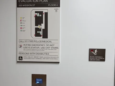Elevator evacuation plan and identification signs on a corridor wall