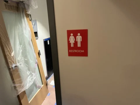 Red all-gender restroom identification sign beside a doorway