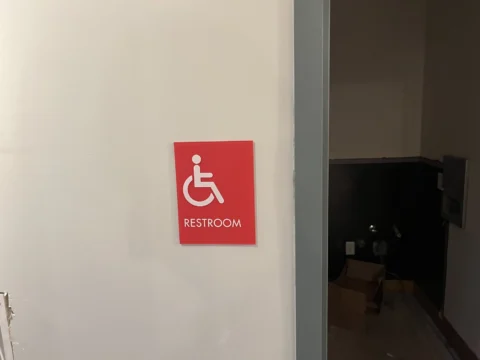 Red wheelchair-accessible restroom sign mounted by an entrance