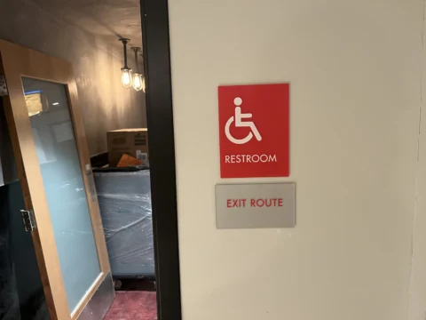 Accessible restroom and exit route signs beside a doorway