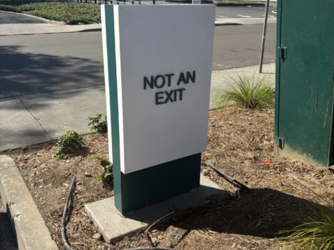 Not an Exit monument sign beside a utility enclosure