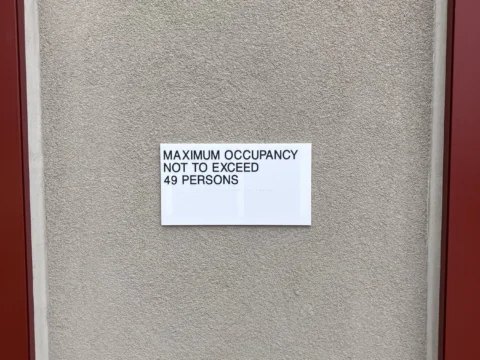Maximum occupancy identification label beside a red doorway